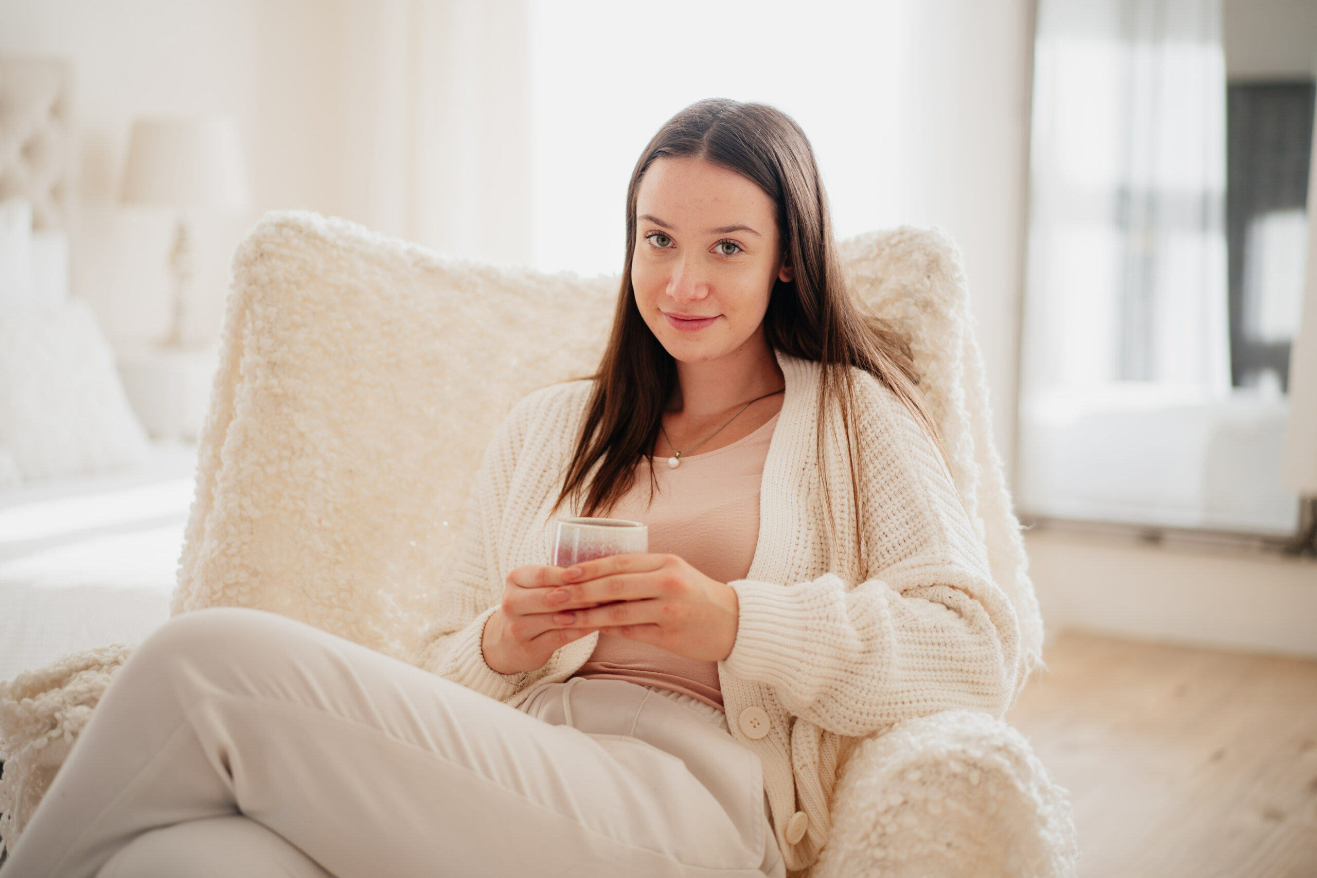 Žena sedící na pohovce doma si prohlíží mobilní telefon